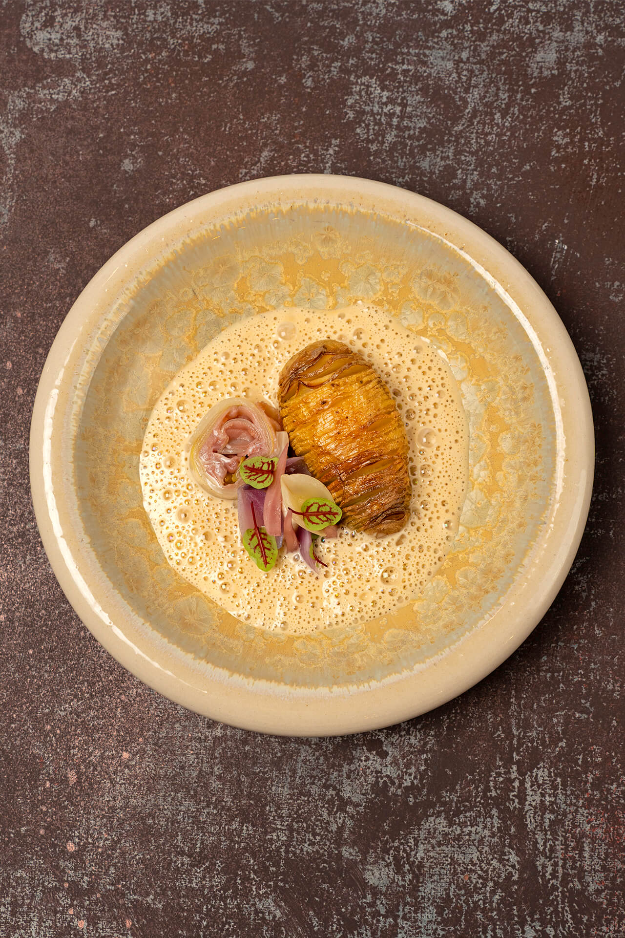 Hasselback aardappel met een rolletje van witlof en serranoham, geitenkaas, ui en cacio e pepe beurre blanc